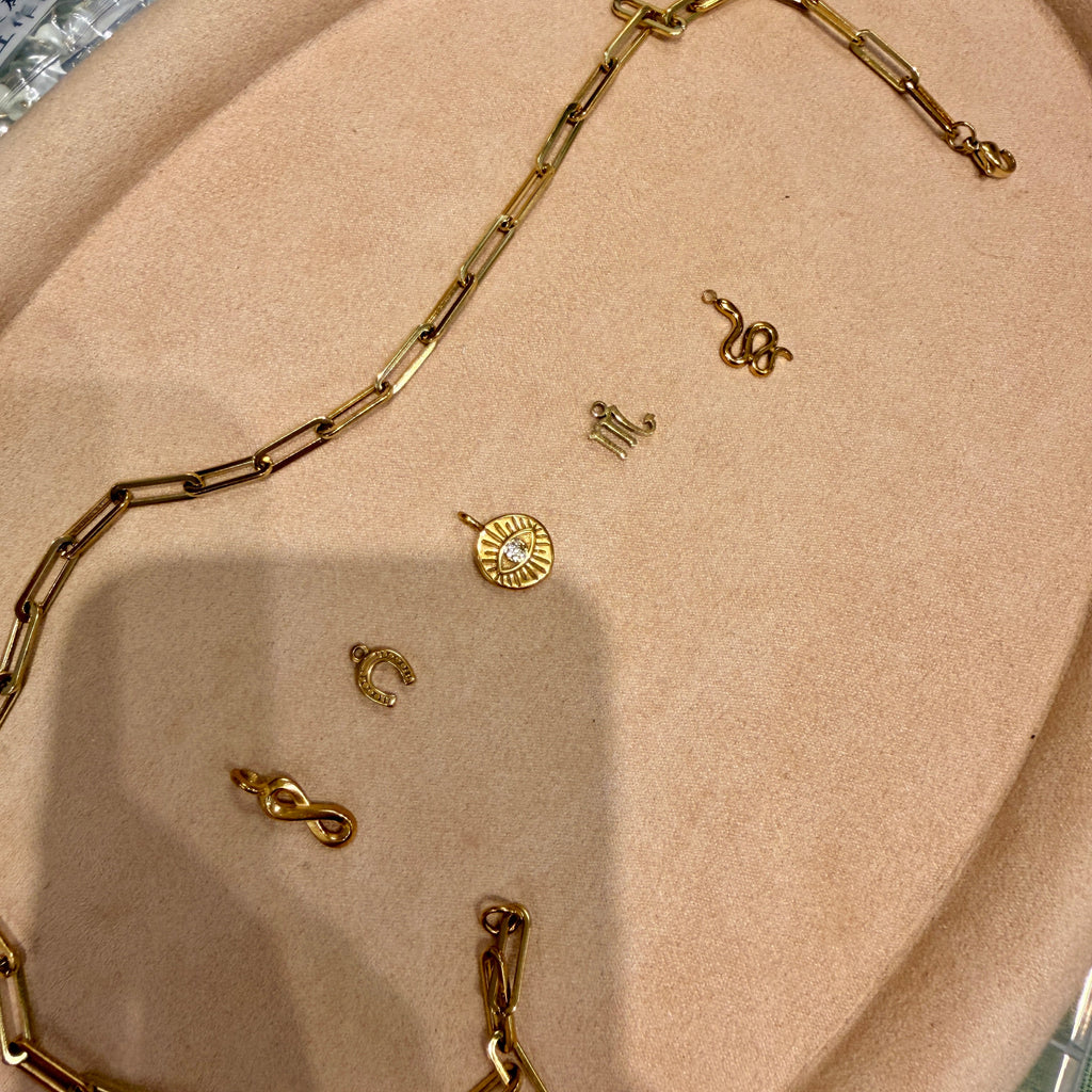 A gold chain necklace and several small gold jewelry pieces arranged on a beige display tray.